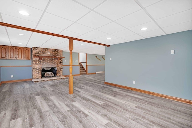 unfurnished living room with a drop ceiling, a brick fireplace, and light hardwood / wood-style flooring