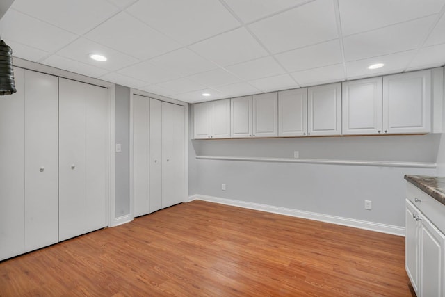 basement with a paneled ceiling and light wood-type flooring