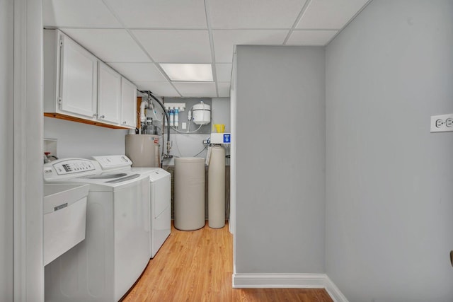 laundry area featuring water heater, light hardwood / wood-style floors, cabinets, and washing machine and clothes dryer