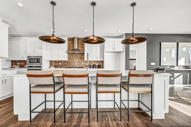 kitchen with appliances with stainless steel finishes, pendant lighting, white cabinetry, wall chimney range hood, and a center island with sink