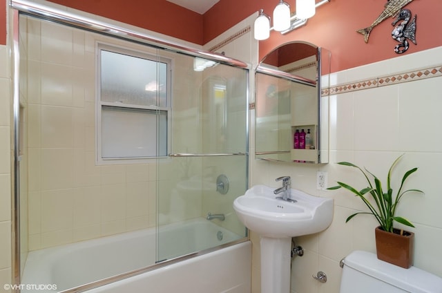 bathroom featuring tile walls, shower / bath combination with glass door, and toilet