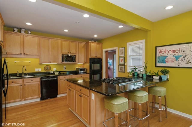 kitchen featuring sink, light hardwood / wood-style flooring, a breakfast bar, black appliances, and dark stone counters