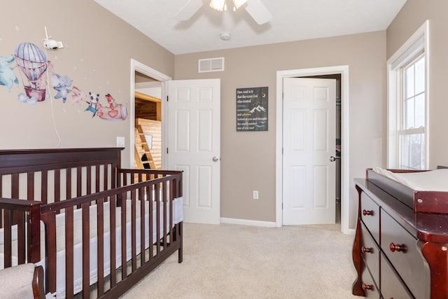 bedroom featuring ceiling fan, light carpet, and a crib