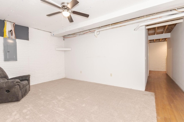 basement with hardwood / wood-style flooring, brick wall, electric panel, and ceiling fan