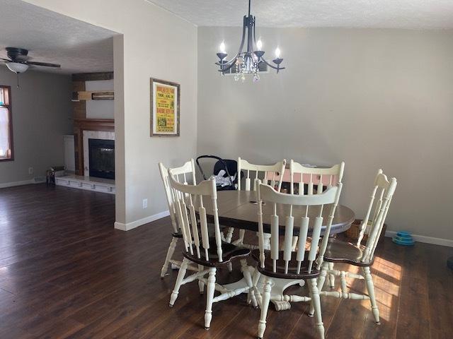 dining area with dark hardwood / wood-style floors, ceiling fan with notable chandelier, and a textured ceiling