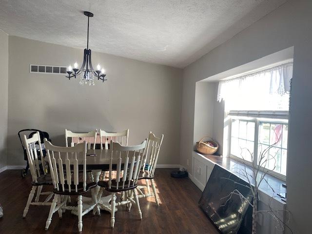 dining room with a notable chandelier, dark wood-type flooring, a textured ceiling, and vaulted ceiling