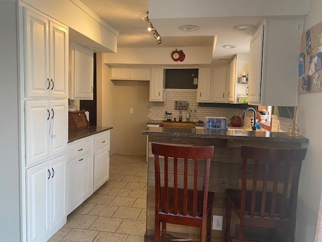 kitchen with tasteful backsplash, white cabinetry, ventilation hood, sink, and kitchen peninsula