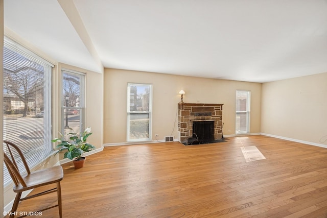 living area featuring visible vents, baseboards, a stone fireplace, and light wood-style flooring