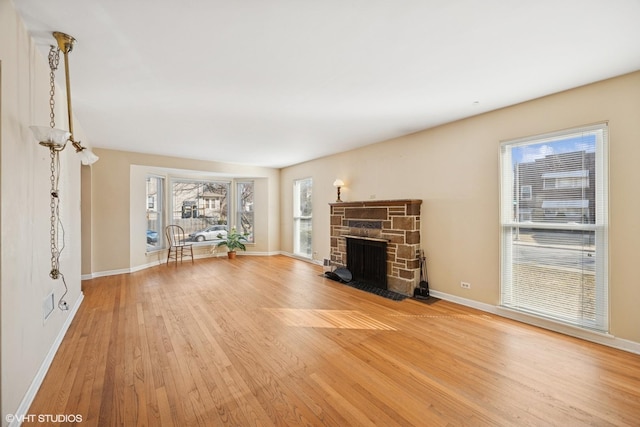 unfurnished living room with a stone fireplace, baseboards, and light wood-type flooring