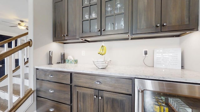 bar with ceiling fan, dark brown cabinetry, beverage cooler, and light stone counters