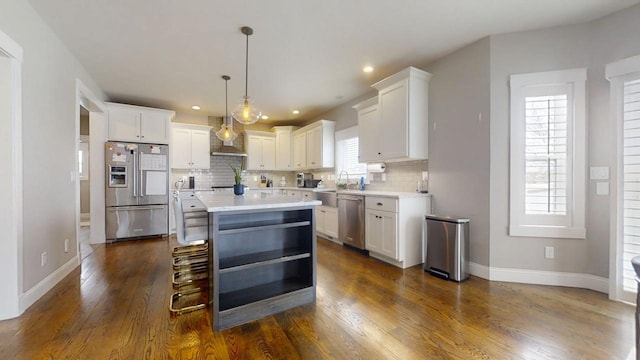 kitchen with appliances with stainless steel finishes, wall chimney range hood, pendant lighting, a kitchen island, and white cabinetry