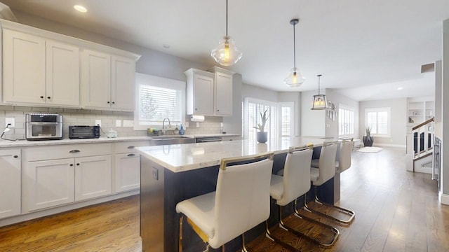 kitchen with light wood-type flooring, pendant lighting, a center island, sink, and white cabinetry