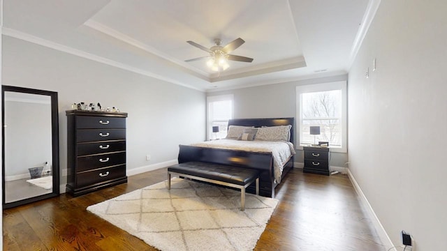 bedroom with a tray ceiling, dark wood-type flooring, ornamental molding, and ceiling fan