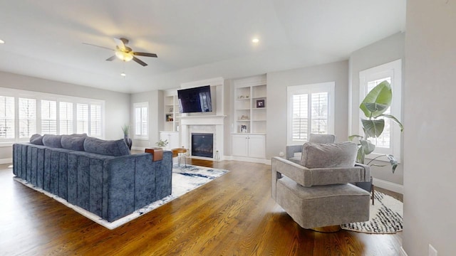 living room with dark wood-type flooring, built in shelves, and ceiling fan