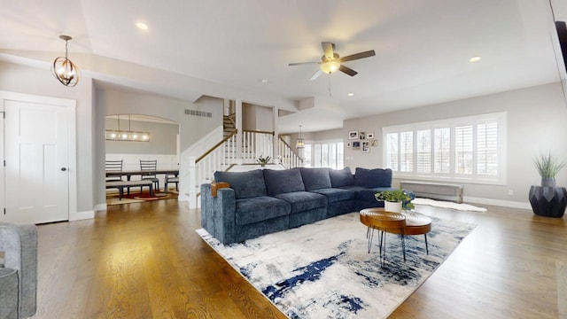 living room with ceiling fan with notable chandelier, vaulted ceiling, and dark wood-type flooring