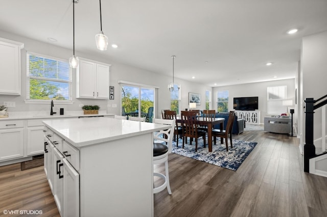 kitchen with pendant lighting, dark wood-type flooring, white cabinetry, a kitchen breakfast bar, and a center island