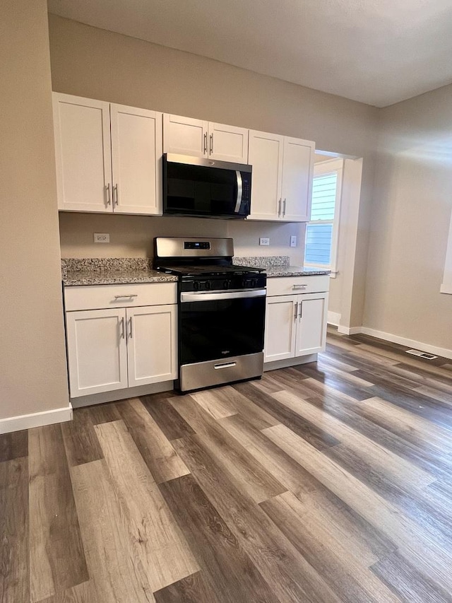 kitchen featuring dark hardwood / wood-style flooring, light stone counters, white cabinets, and appliances with stainless steel finishes