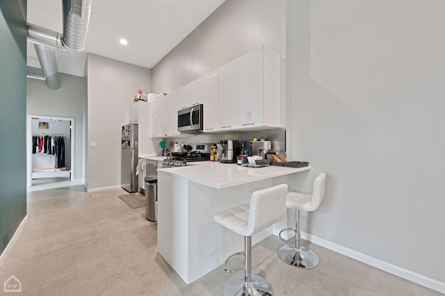 kitchen featuring a breakfast bar, kitchen peninsula, white cabinets, stainless steel appliances, and backsplash