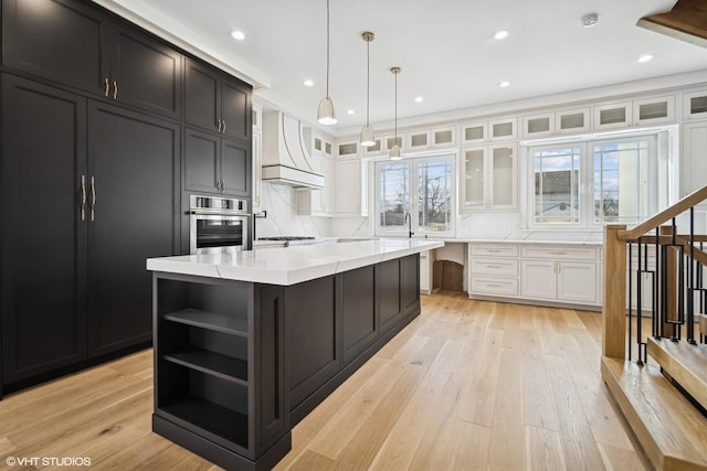 kitchen with light stone counters, white cabinets, a kitchen island, custom exhaust hood, and oven