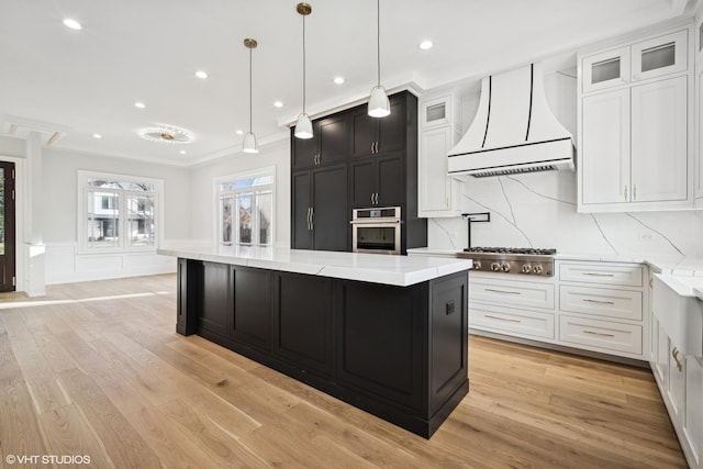 kitchen with hanging light fixtures, stainless steel appliances, custom range hood, white cabinets, and a kitchen island