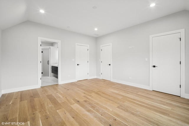 unfurnished bedroom with vaulted ceiling, connected bathroom, and light wood-type flooring