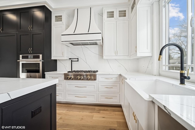 kitchen with light stone countertops, appliances with stainless steel finishes, custom range hood, and white cabinets