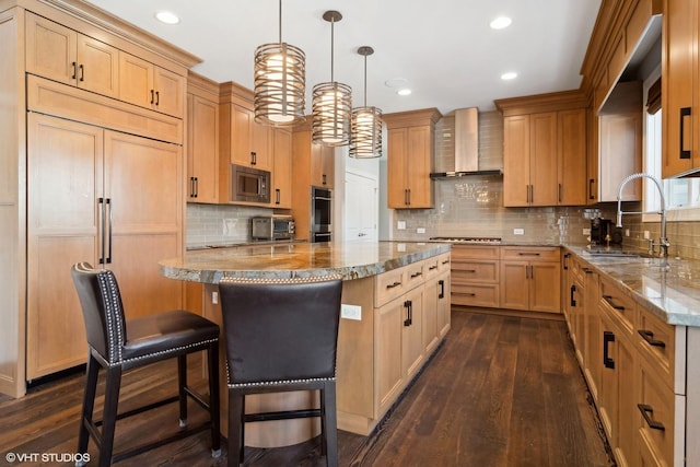 kitchen with a sink, wall chimney exhaust hood, hanging light fixtures, built in appliances, and a center island