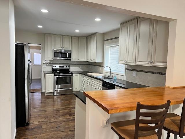 kitchen featuring stainless steel appliances, sink, butcher block countertops, kitchen peninsula, and a healthy amount of sunlight