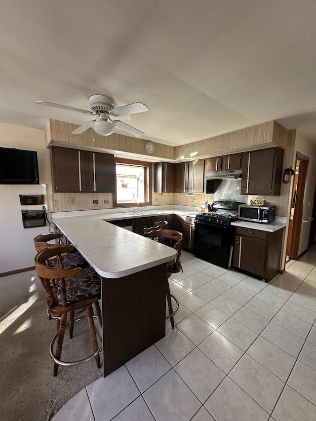 kitchen featuring a breakfast bar, black gas range oven, ceiling fan, kitchen peninsula, and dark brown cabinets