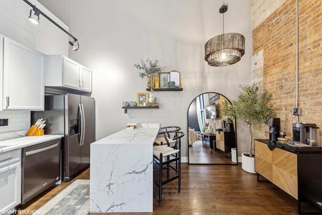 kitchen featuring appliances with stainless steel finishes, a towering ceiling, white cabinetry, hanging light fixtures, and light stone countertops