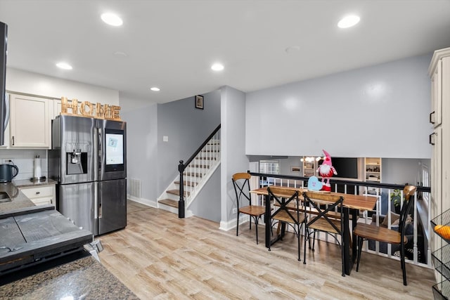 kitchen with white cabinetry, stainless steel fridge, dark stone counters, and light wood-type flooring