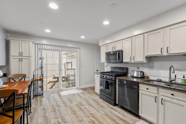 kitchen with white cabinetry, sink, dark stone countertops, light hardwood / wood-style floors, and black appliances