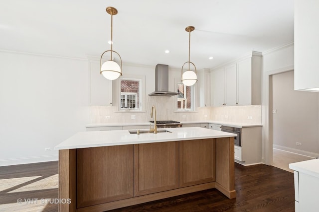 kitchen featuring white cabinets, decorative light fixtures, a center island with sink, and wall chimney range hood