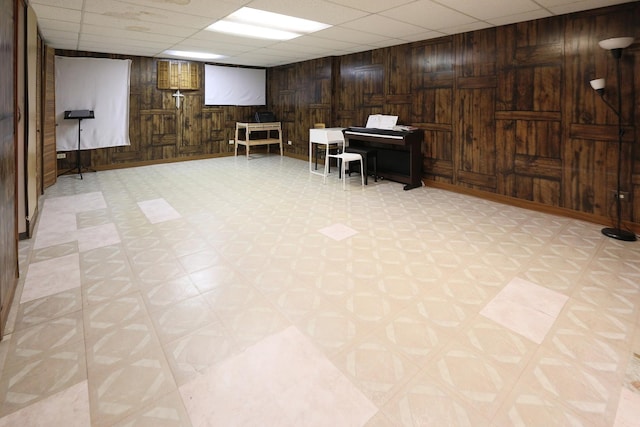 basement featuring a drop ceiling and wood walls