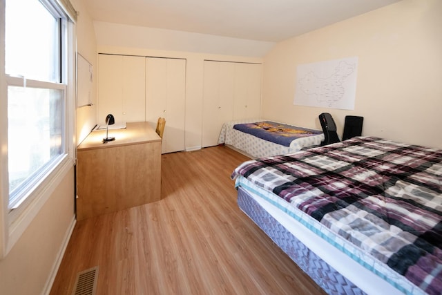 bedroom featuring lofted ceiling, light hardwood / wood-style flooring, and multiple closets