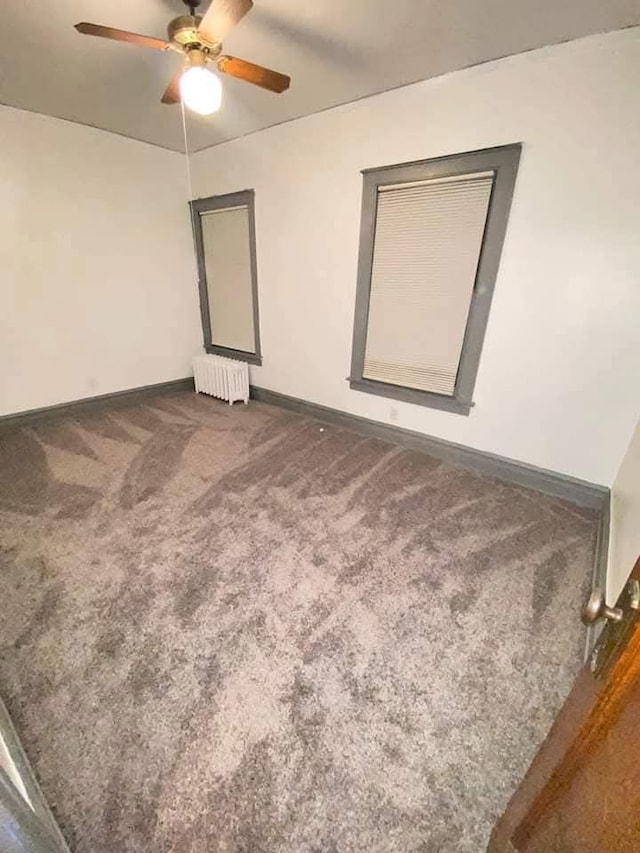 carpeted empty room featuring ceiling fan and radiator