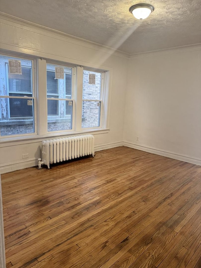 empty room featuring hardwood / wood-style flooring, crown molding, radiator, and a textured ceiling