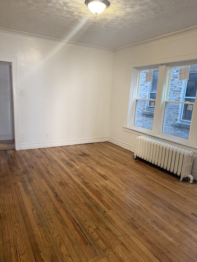 empty room featuring hardwood / wood-style flooring, ornamental molding, radiator heating unit, and a textured ceiling