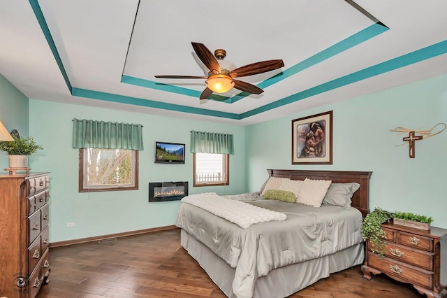 1401 Rolling Pass, Beecher, IL 60401 - bedroom with a tray ceiling, baseboards, dark wood-style flooring, a glass covered fireplace, and a ceiling fan
