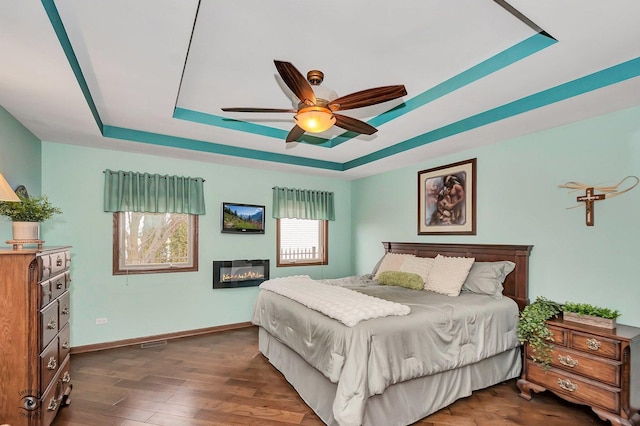 bedroom featuring ceiling fan, dark hardwood / wood-style flooring, and a tray ceiling