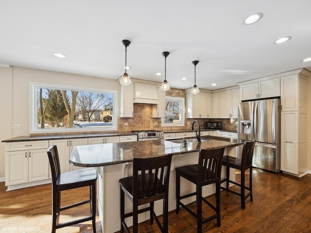 kitchen featuring decorative light fixtures, custom exhaust hood, appliances with stainless steel finishes, a sink, and an island with sink