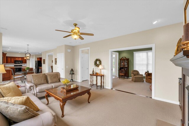 living area featuring light carpet, ceiling fan with notable chandelier, recessed lighting, a fireplace, and baseboards