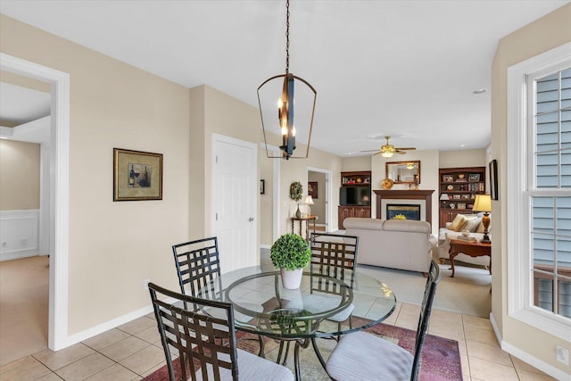 dining area featuring light tile patterned floors, a glass covered fireplace, ceiling fan with notable chandelier, and built in shelves