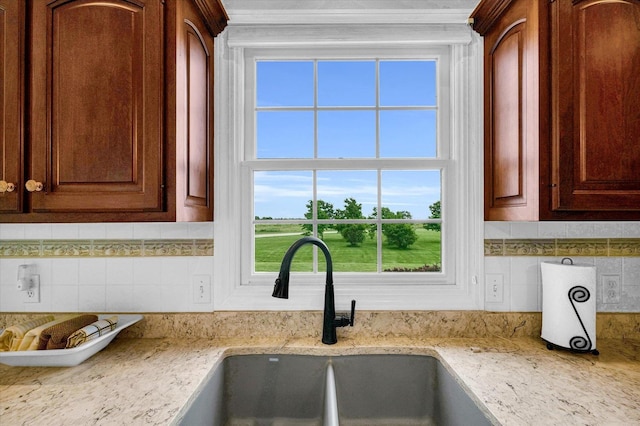 kitchen featuring light stone countertops, tasteful backsplash, and a sink