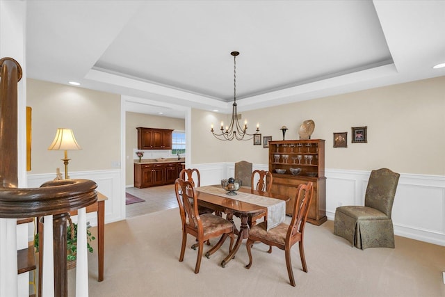 dining area with a raised ceiling, light colored carpet, and wainscoting