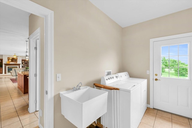 laundry room featuring laundry area, a fireplace, light tile patterned flooring, washer and dryer, and a sink