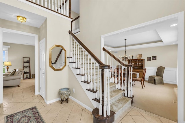 stairs with a chandelier, carpet floors, wainscoting, tile patterned floors, and a raised ceiling