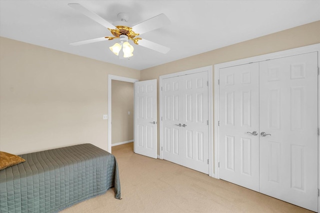 bedroom featuring baseboards, a ceiling fan, multiple closets, and light carpet