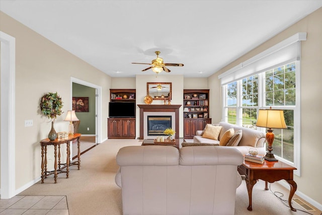 living area with a glass covered fireplace, light colored carpet, baseboards, and a ceiling fan