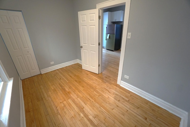 unfurnished bedroom featuring stainless steel refrigerator and light wood-type flooring